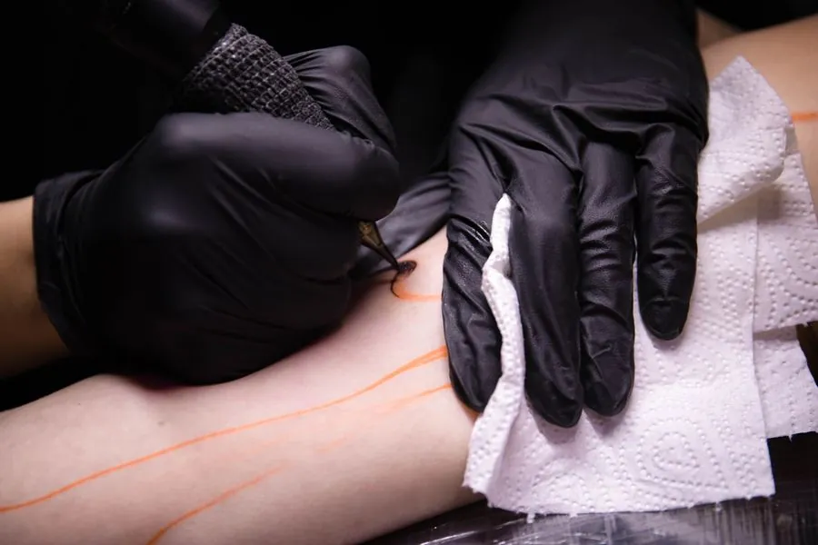 Gloved hands mapping a line on skin before tattooing